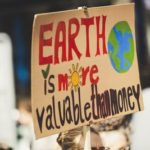 person holding sign that says "Earth is more valuable than money"