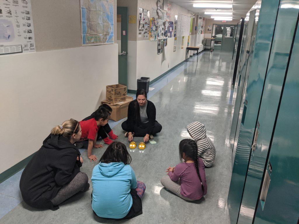 Delivery team Courtney and a teacher playing with beebots in the hall of a school