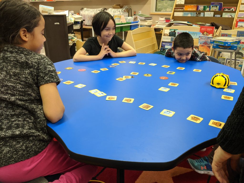 some students gathered around a table playing beebots.