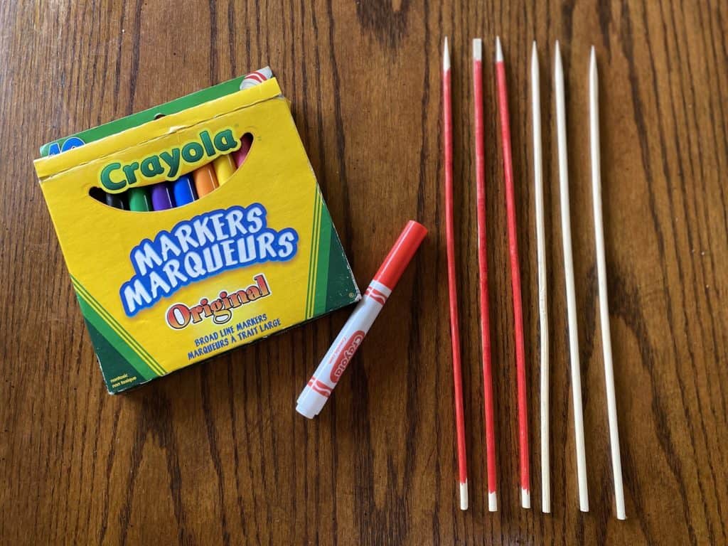 Crayola markers laying beside coloured sticks on a wooden table.