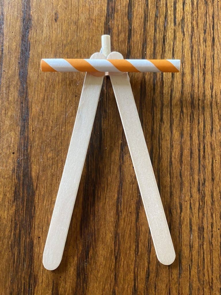 A short orange and white stripped straw laying across two popsicle sticks.