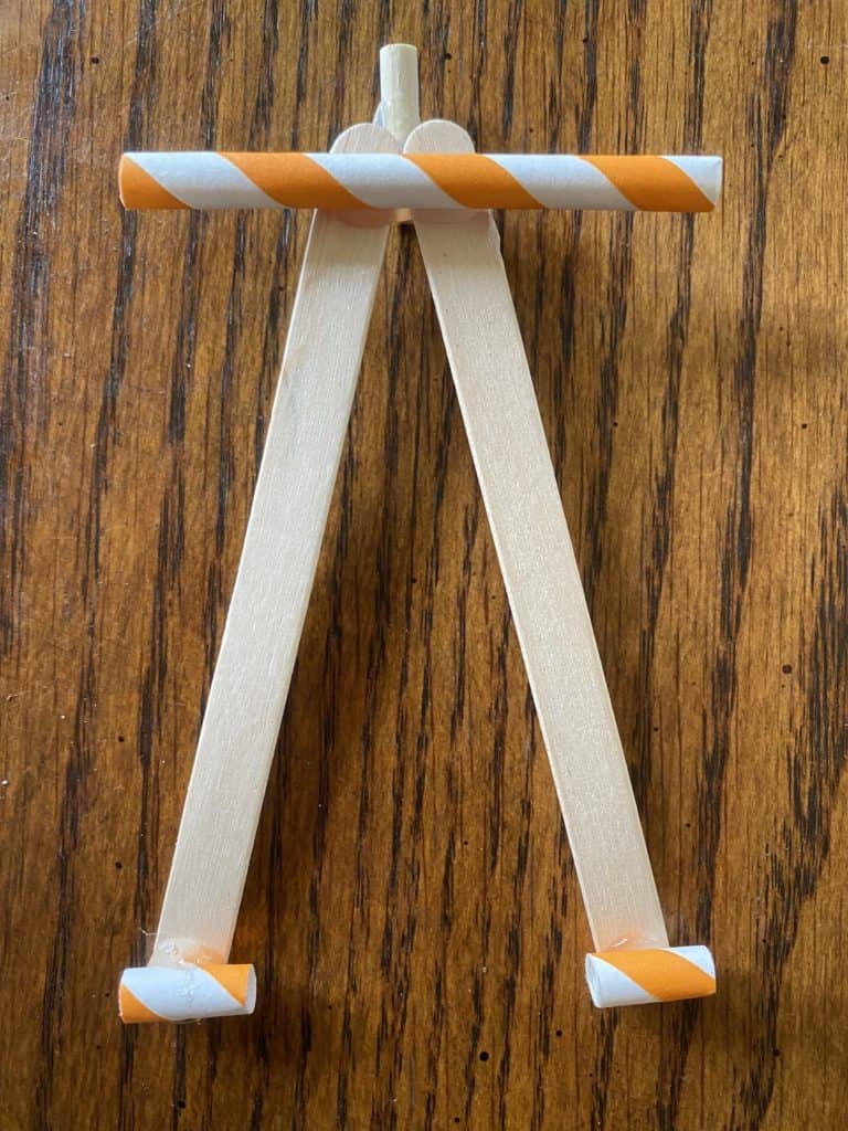 Orange and white straws laying across the top and bottom of two popsicle sticks.