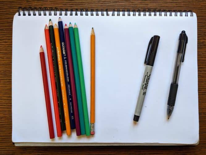 A blank piece of paper with pencil crayons, as well as a marker and pen.