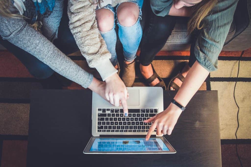 3 people sitting in front of an illuminated computer. All 3 are pointing at it.