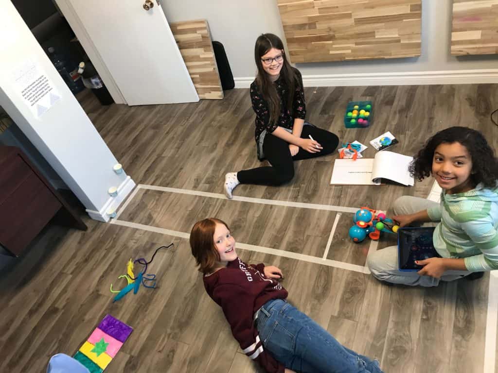 Three students sitting on the floor of the Lindsay Makerspace using a Dash and Dot robot.