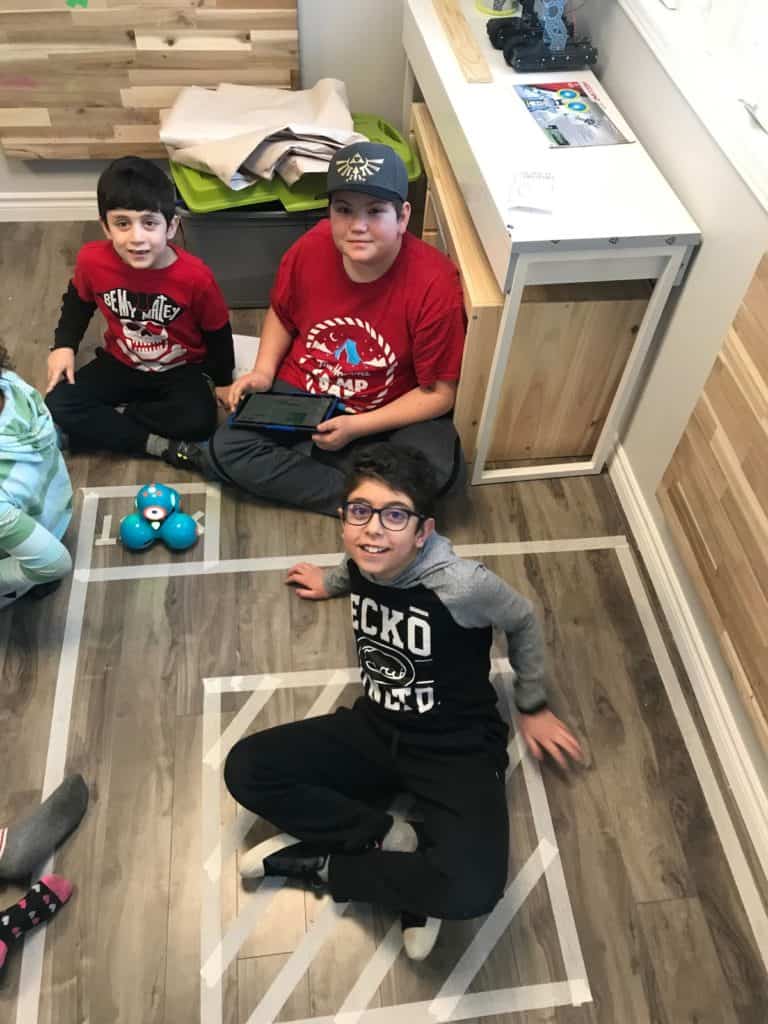 Students sitting on the floor of the Lindsay Makerspace in an obstacle course and a Dash and Dot robot.