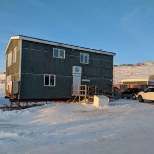 A dark building with snow on the ground, where the Iqaluit Makerspace is.