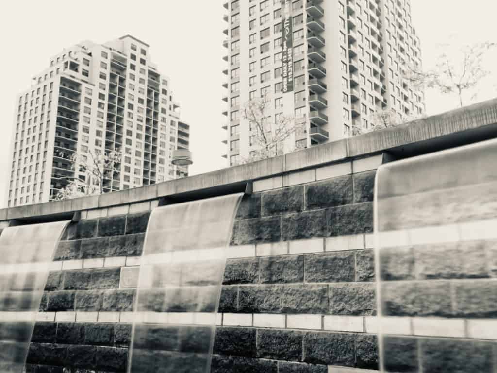 A photograph of 3 waterfalls, with buildings in the background.