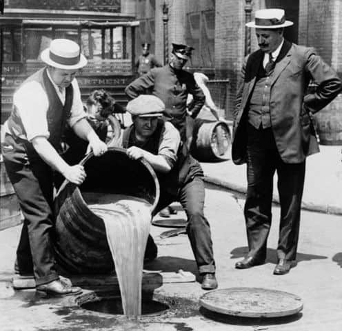 Men dumping alcohol from a barrel into the sewer during prohibition.