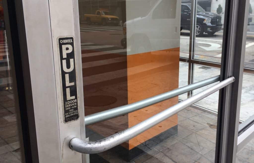 A door with a full horizontal handle bar across it and a pull sign.
