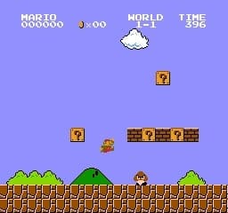 Level 1-1 of Super Mario Bros. with bricks and questions blocks and Mario jumping up to avoid a Goomba.