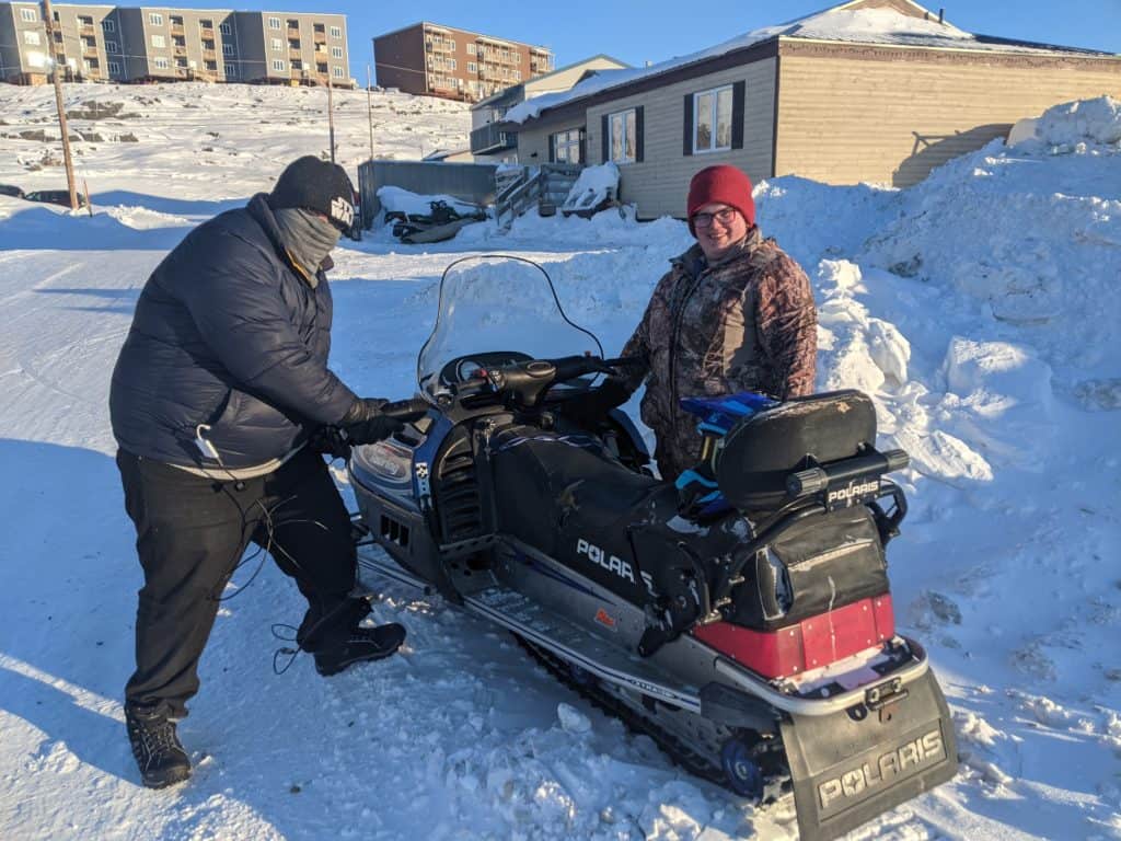 Nunavut Game Jam, two people are shown standing beside a snowmobile.