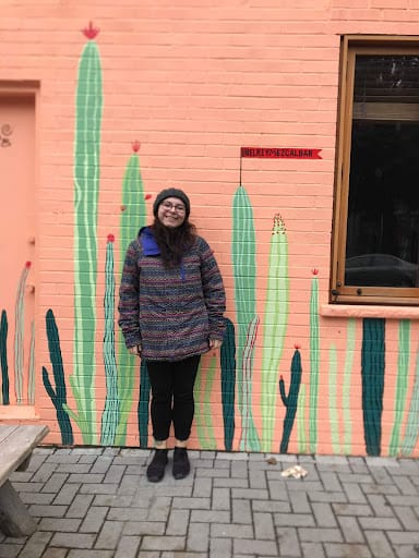 Digital content coordinator, Hailey, standing in front of a wall with cacti painted on it.